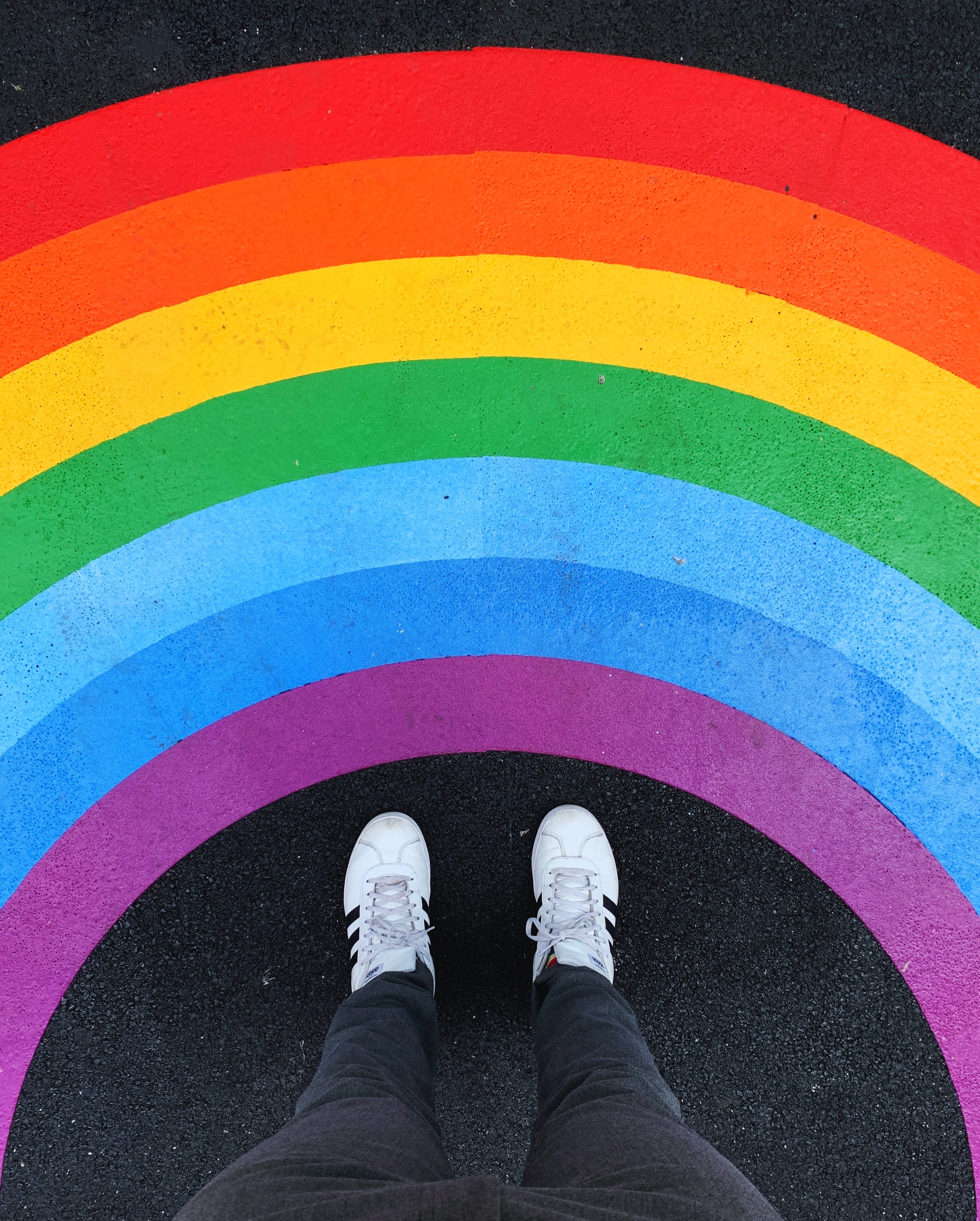 Vielfalt – Füße in weißen Sneakern vor regenbogenfarbigen Boden
