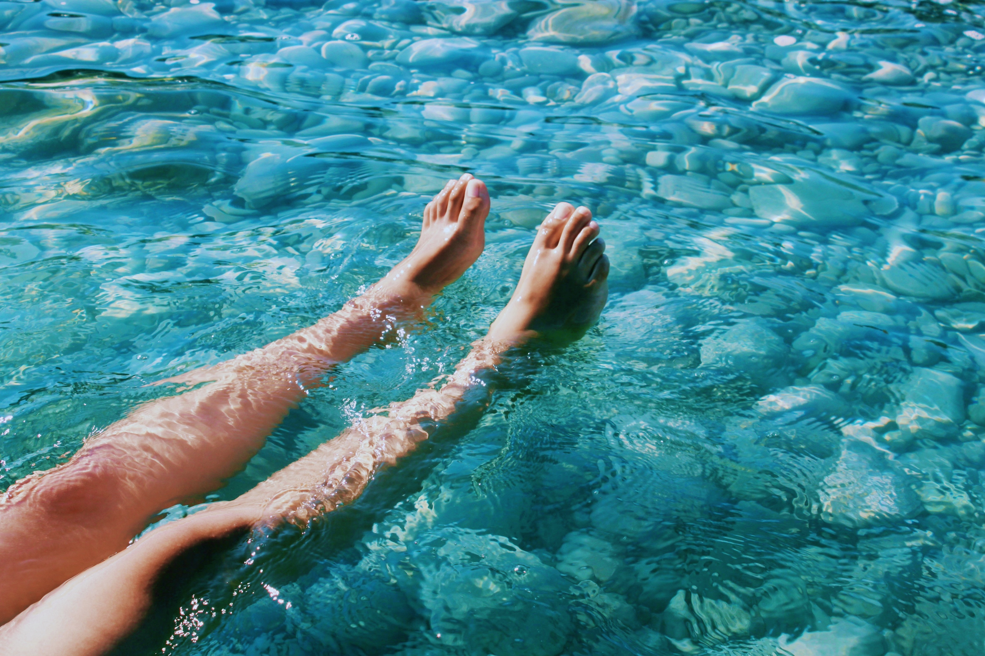 Nackte Beine und Füße in transparent-blauem Wasser über steinigem Grund
